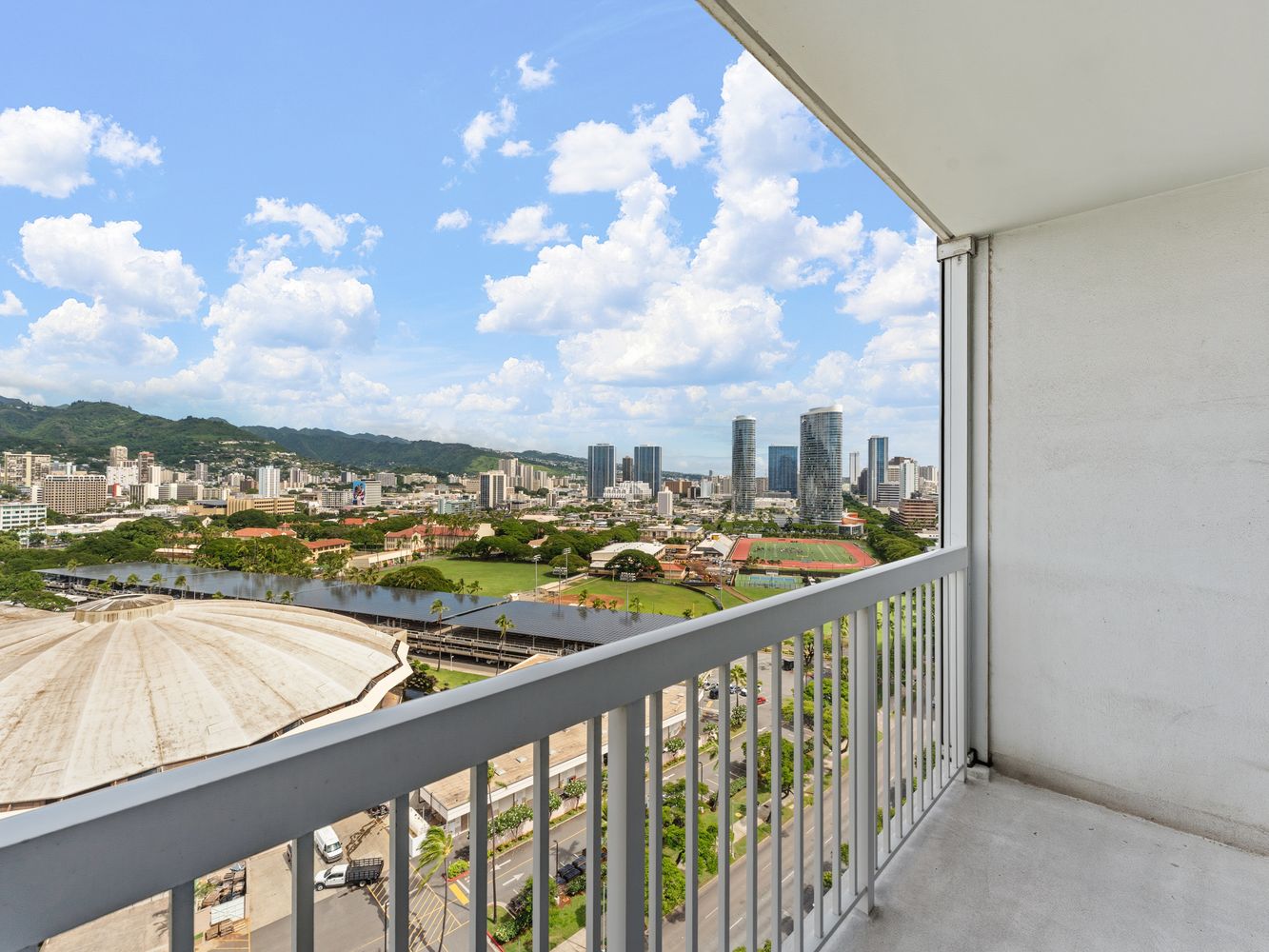 Balcony view over a circular roof and athletic fields with green mountains beyond