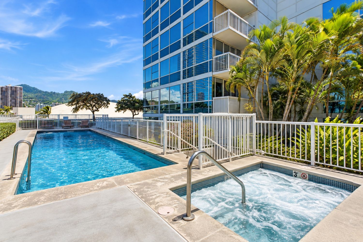 Pool deck with a rectangular swimming pool, hot tub, palm trees and mountain views